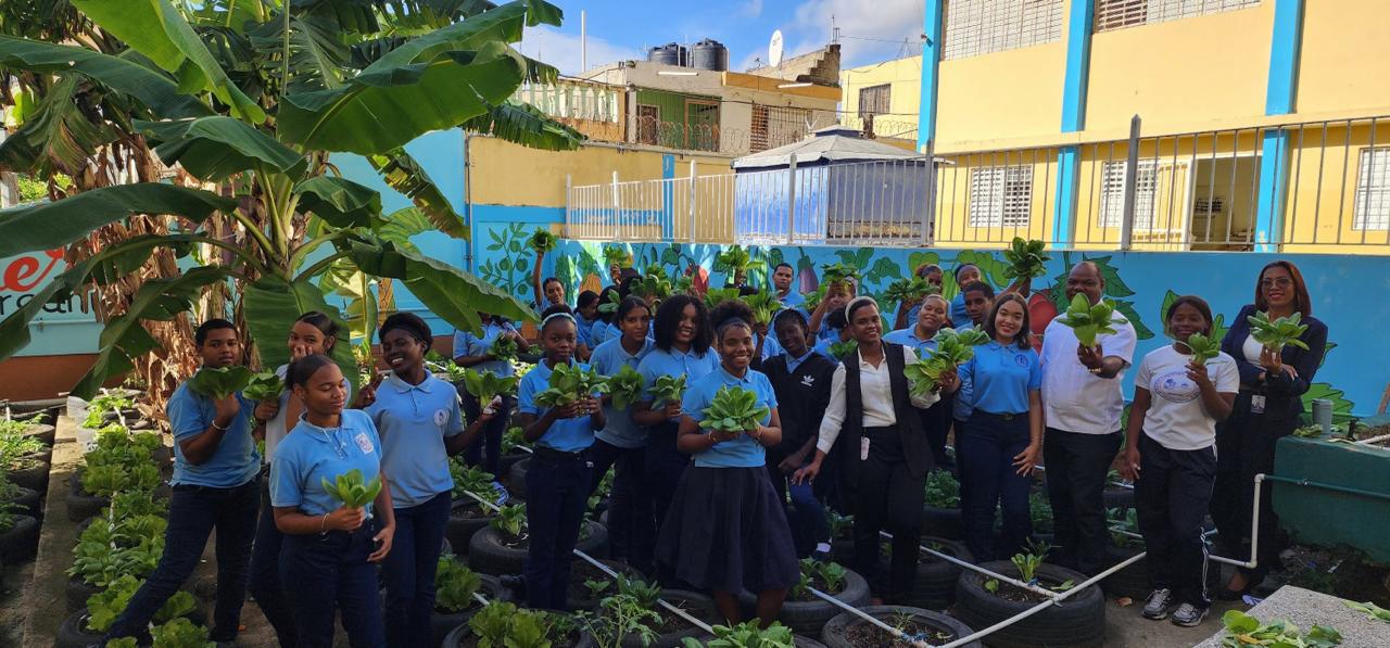 Students and staff standing among rows of tire planters, each holding a head of lettuce grown in the school garden.